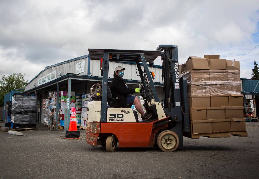 A volunteer helps more move pallets outside of the Sky Valley Food Bank on Friday, May 15, 2020 in Monroe, Wa. (Olivia Vanni / The Herald)