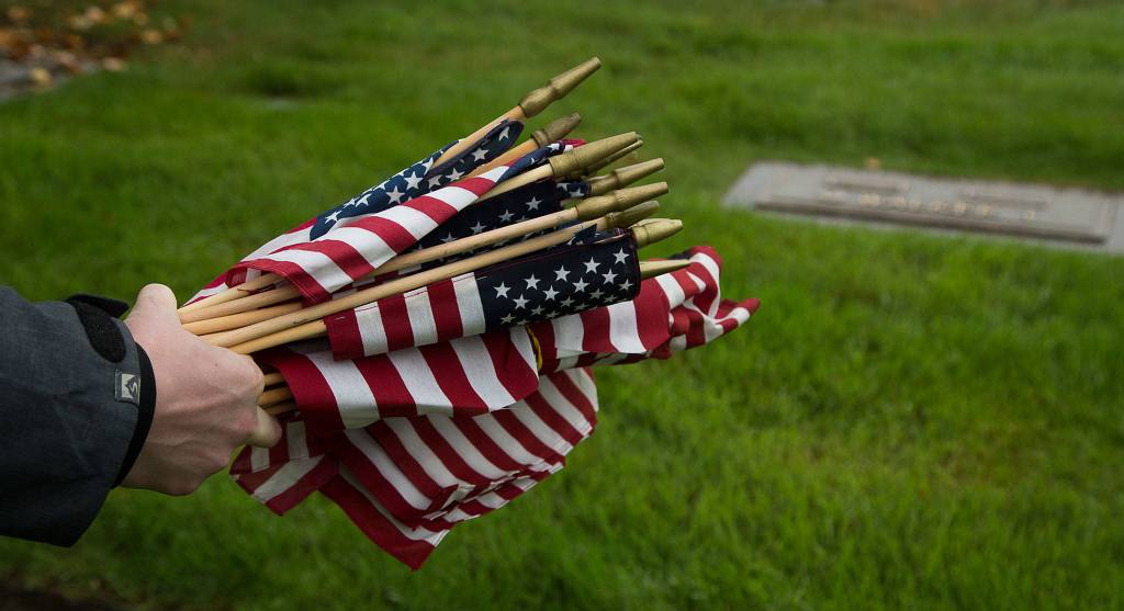 Former U.S. Marine Sean Hunt grabs a handful of flags to place on veteran grave markers at Floral Hills Cemetery on Memorial Day. (Andy Bronson / The Herald)