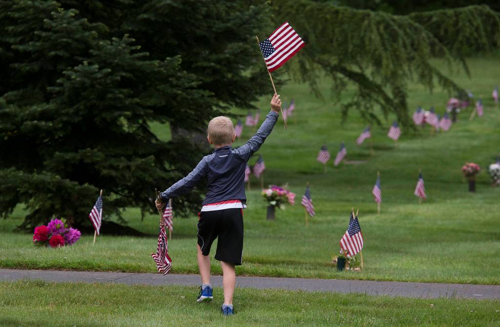 Shane McKenzie, 6, waves a flag as he searches Floral Hills cemetery for graves without the markers. (Andy Bronson / The Herald)