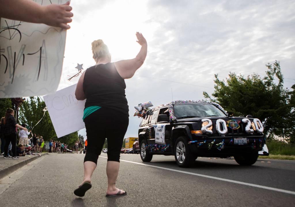 Bree Brinde holds a sign and waves at high school graduates as they drive along 108th Street in the Marysville-Tulalip All High School Senior Parade on Friday, May 29, 2020 in Marysville, Wa. (Olivia Vanni / The Herald)