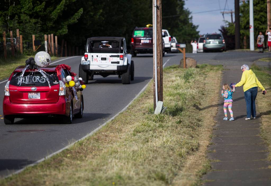 People wave and cheer as local high school graduates drive by during the Marysville-Tulalip All High School Senior Parade on Friday, May 29, 2020 in Marysville, Wa. (Olivia Vanni / The Herald)