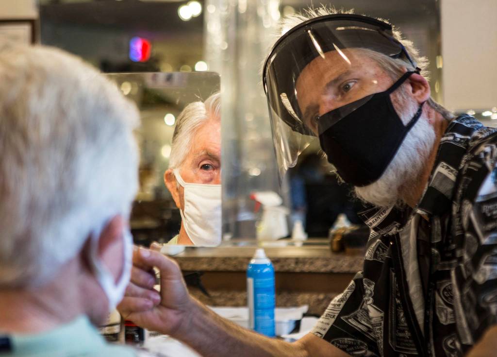 Steve Iblings, outfitted in a mask and a protective face shield, holds a mirror up for Bob DeFrang to look at his hair after his first haircut in three months Saturday in Lake Stevens. (Olivia Vanni / The Herald)