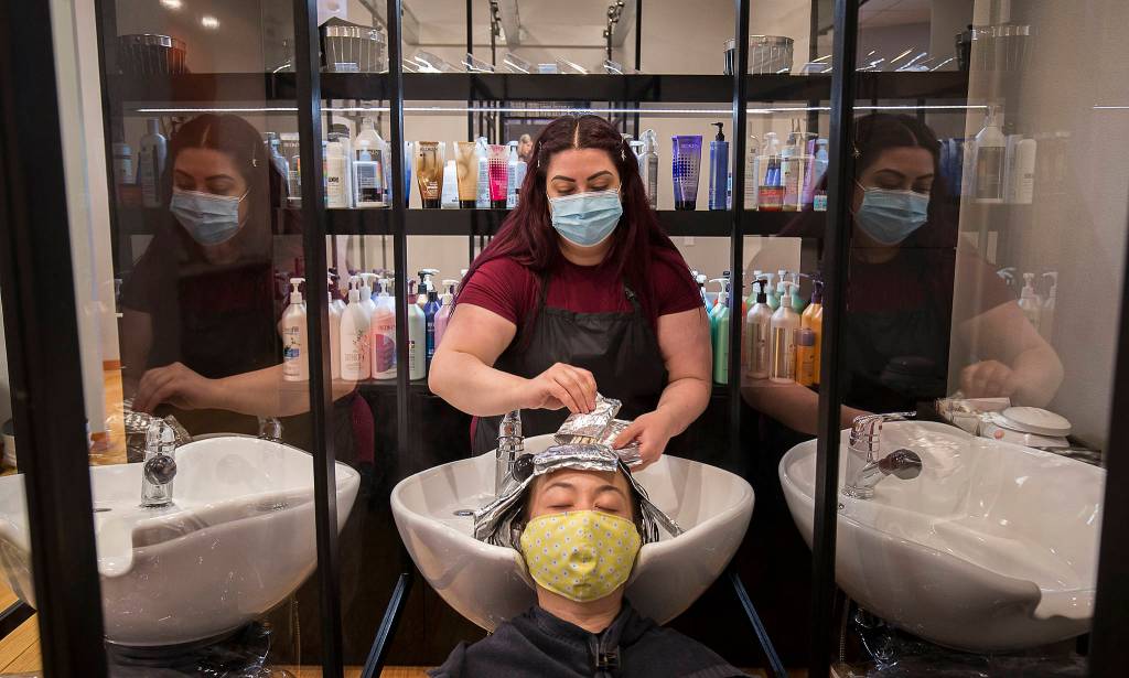 Glass partitions separate hair washing stations as Emily Lothchomphou removes foil wraps from Waan Bartletts hair at Salon Zuberenz in Lynnwood. (Andy Bronson / The Herald)