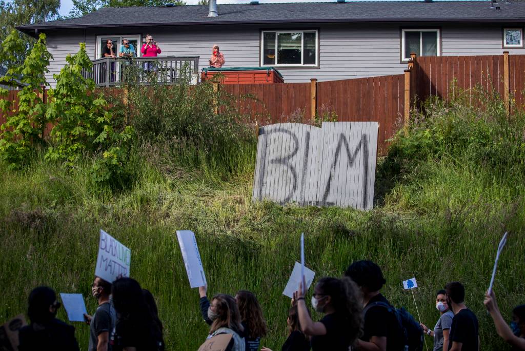 People watch from their deck as protesters make their way along Mukilteo Speedway during the Black Lives Matter protest on Sunday in Mukilteo. (Olivia Vanni / The Herald)