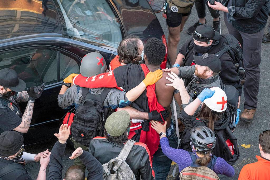 An injured man is taken away from the scene after a gunman drove toward protesters Sunday in Seattle. (Dean Rutz/The Seattle Times via AP)