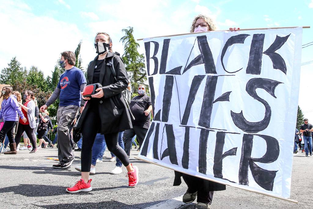 Protesters hold a large banner as they march through Marysville Thursday, in an effort to speak out against racism. (Kevin Clark / The Herald)