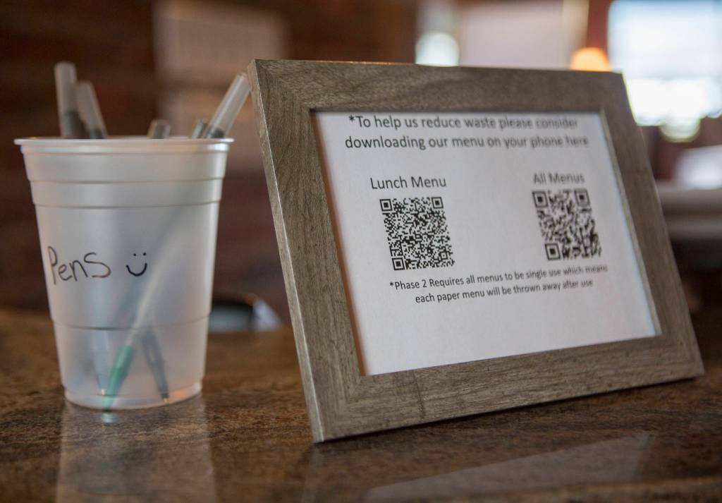 A cup with clean pens and a sheet with a QR code for a virtual menu sit on the host desk at Lombardis Italian Restaurant on Saturday in Everett. (Olivia Vanni / The Herald)