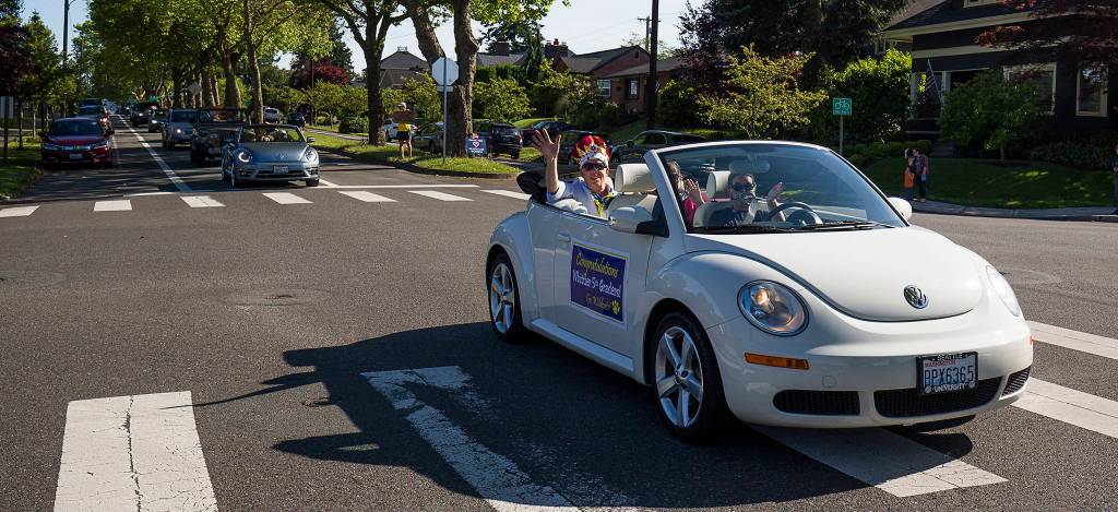 Wearing a crown, music teacher George Spencer waves from a white Volkswagen Bug convertible as the car leads a parade for Whittier Elementary teachers and staff on Wednesday in Everett. Spencer is retiring after 36 years with the Everett School District. (Andy Bronson / The Herald)