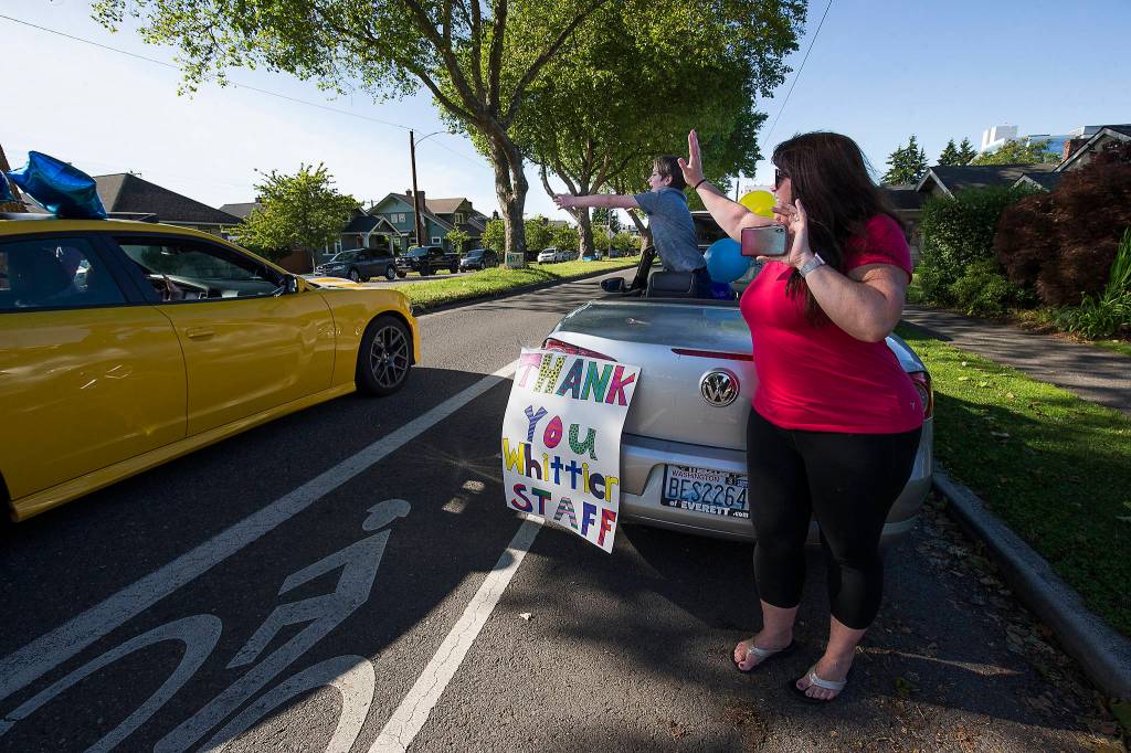 Jen Russell and Lachlan Chambers wave and cheer Wednesday as a parade for Whittier Elementary teachers and staff rolls by on Colby Avenue in Everett. (Andy Bronson / The Herald)