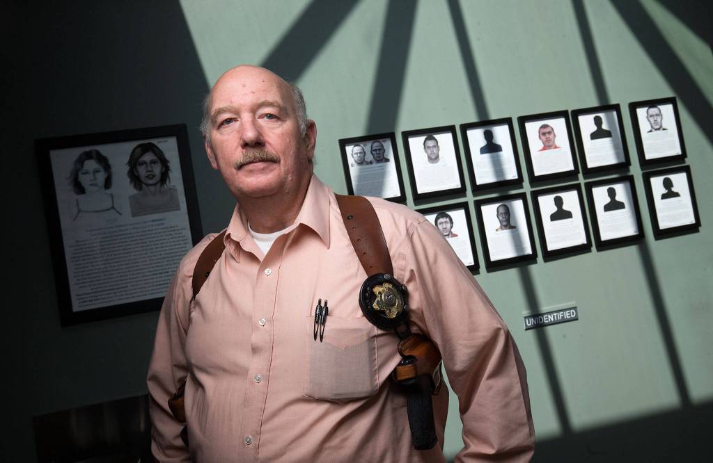 Jim Scharf, a detective for the Snohomish County Sheriffs Office, stands in front of a display for unidentified persons on a wall at the Snohomish County Medical Examiners Office in 2018 in Everett. Behind his right shoulder is the artist rendering of Precious Jane Doe. (Andy Bronson / Herald file)
