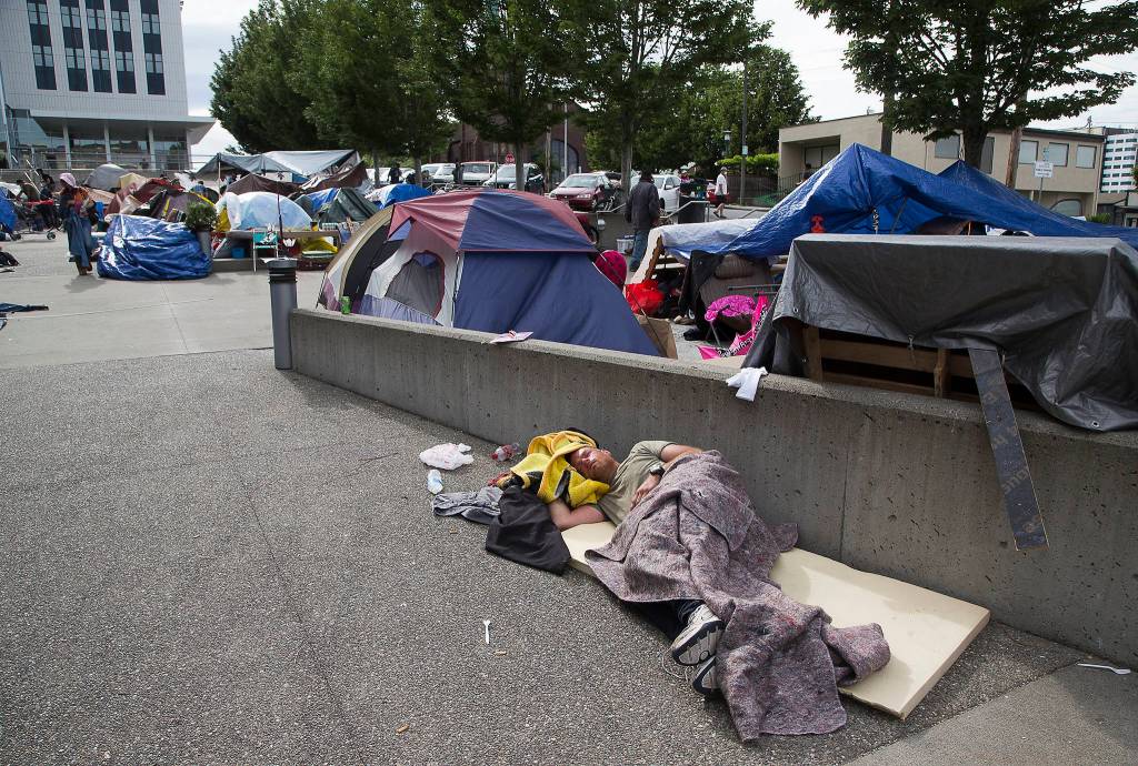 A man sleeps on a pad in an encampment for the homeless on the plaza at Wall Street and Oakes Avenue in Everett. (Andy Bronson / The Herald)