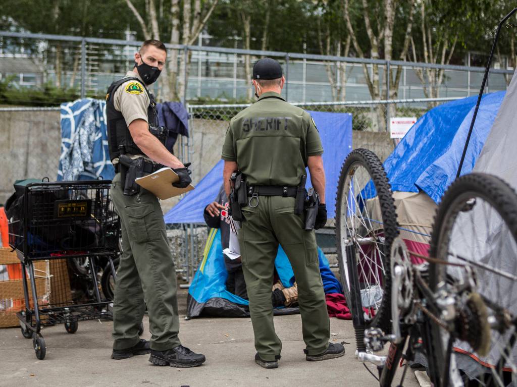 Sheriffs deputies walk through a downtown homeless camp, handing out resource flyers on Thursday in Everett. They were informing people that they will need to be moved out on July 5 no later than 5 p.m. (Olivia Vanni / The Herald)