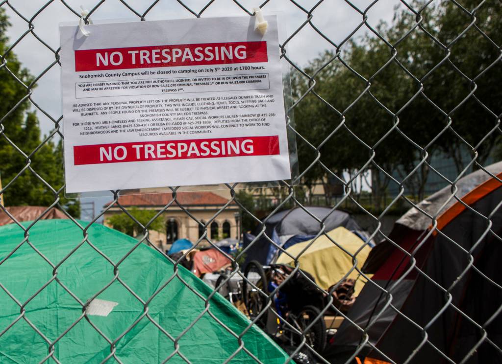 A sign of warning hangs on the fence surrounding the homeless encampment in downtown Everett on Thursday. (Olivia Vanni / The Herald)