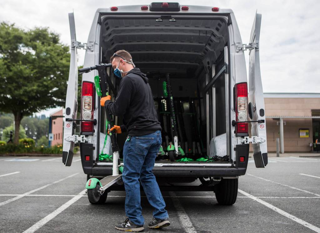 A Lime scooter employee loads scooters in need of charging into a van Wednesday in Bothell. (Olivia Vanni / The Herald)