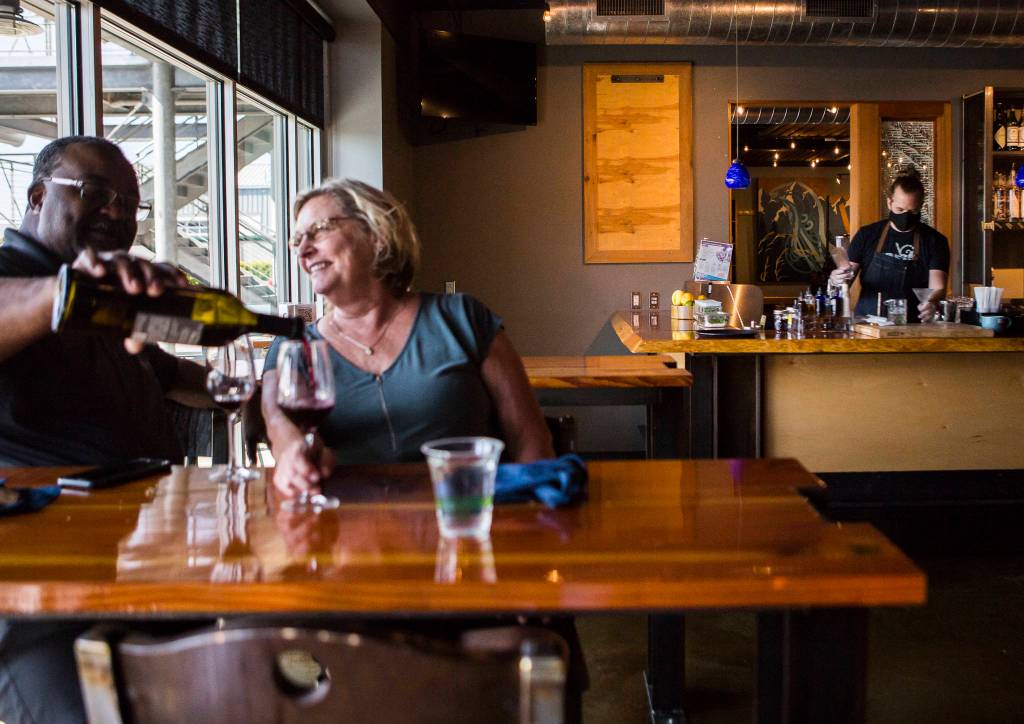 David and Juanita Gibson, left, enjoy a bottle of wine while Kyle Gavin works on cocktail orders Friday at Bluewater Distilling in Everett. (Olivia Vanni / The Herald)