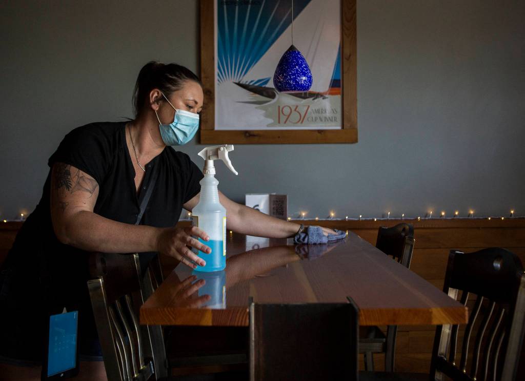 Madison Bauer sanitizes a table at Bluewater Distilling in between customers Friday in Everett. (Olivia Vanni / The Herald)