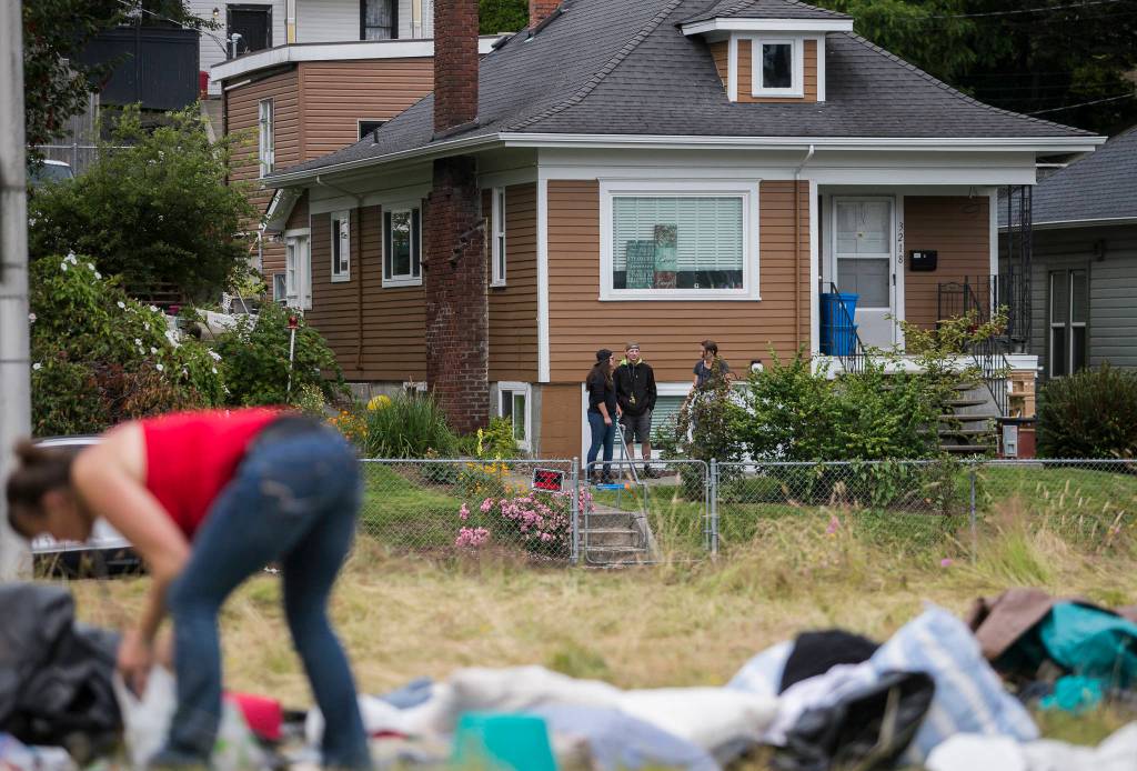 Neighbors watch as people clean and gather their belongings at a homeless encampment on Thursday in Everett. (Olivia Vanni / The Herald)