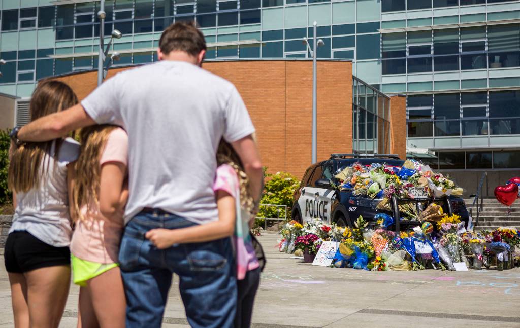 Ryan Murphy holds his daughters, Peyton, Teegan and Paisley, as they pay their respects Tuesday to the Bothell police officer who was killed Monday night. (Olivia Vanni / The Herald)