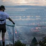 Neighbors spray down smoking brush along Grand Avenue as the fire burns along Marine View Drive on Thursday, July 16, 2020 in Everett, Wa. (Olivia Vanni / The Herald)