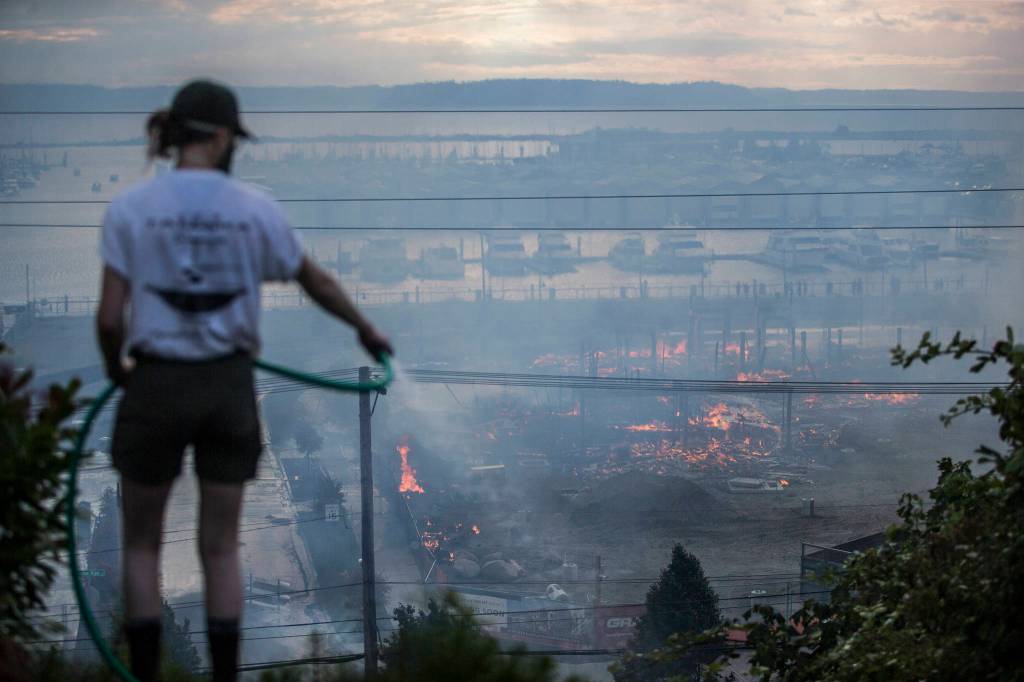 Neighbors spray down smoking brush along Grand Avenue as the fire burns along Marine View Drive on Thursday, July 16, 2020 in Everett, Wa. (Olivia Vanni / The Herald)