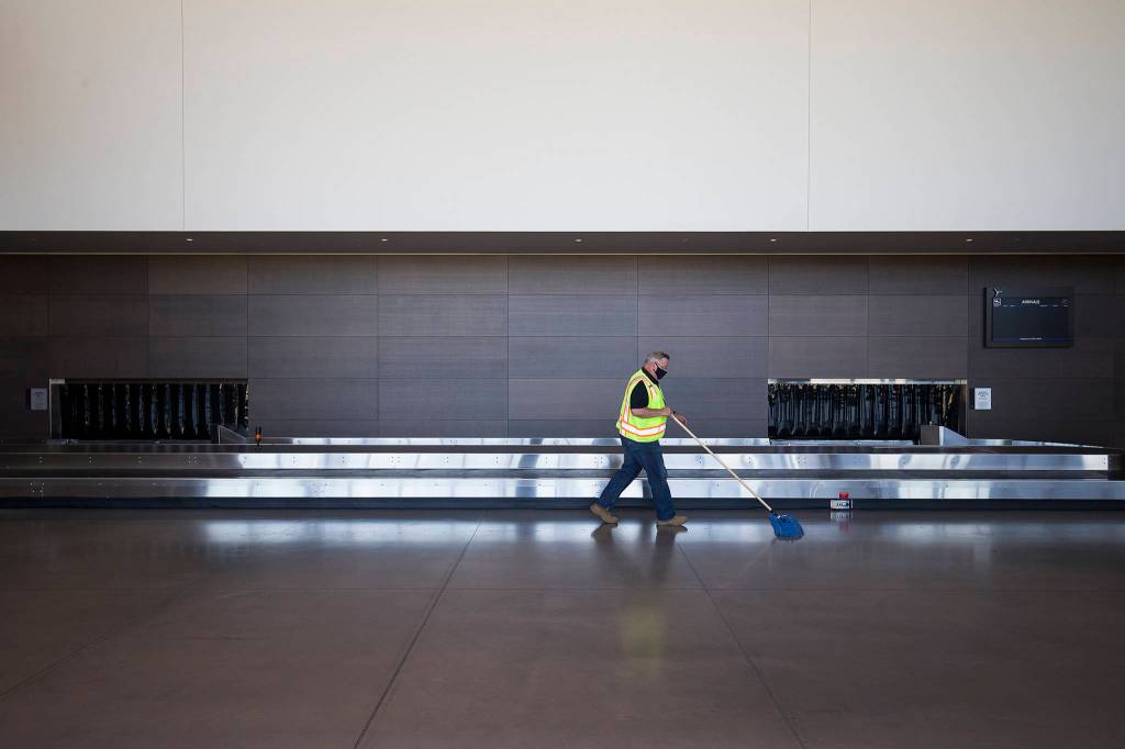 Terminal duty manager Tom Hoctor sweeps the baggage pickup area as he helps prepare for passenger service to return Saturday at Paine Field. (Andy Bronson / The Herald)