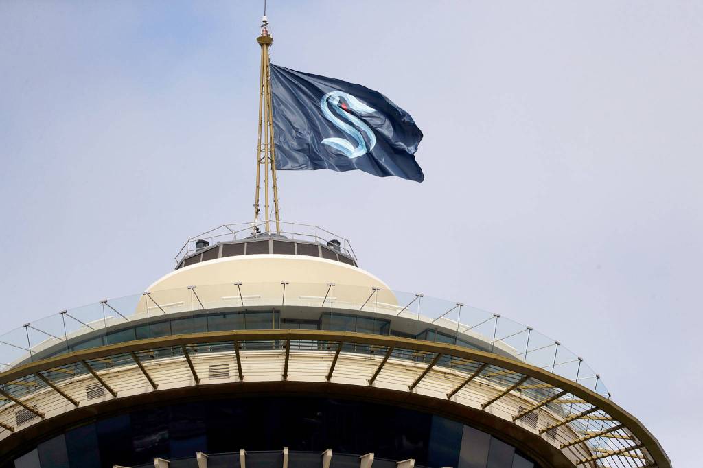 A flag with the new logo for the newly named Seattle NHL team, the Seattle Kraken, flies atop the iconic Space Needle Thursday, July 23, 2020, in Seattle. The hockey expansion franchise unveiled its nickname Thursday, ending 19 months of speculation about whether the team might lean traditional or go eccentric with the name for the leagues 32nd team. Seattles colors are a deep dark blue with a lighter shade of blue as a complement. (AP Photo/Elaine Thompson)