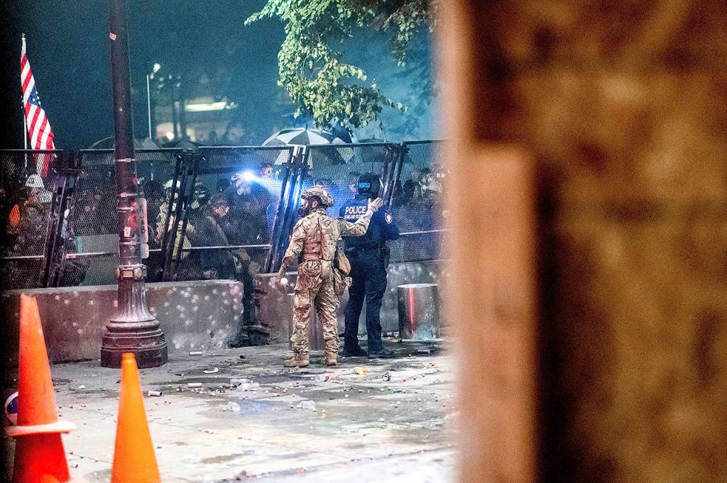 As protesters gather behind a fence, federal officers work to maintain a perimeter in front of the Mark O. Hatfield U.S. Courthouse on Friday in Portland. (AP Photo/Noah Berger)