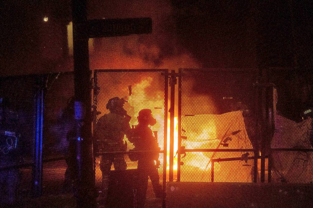 Federal officers guard the Mark O. Hatfield U.S. Courthouse as a fire lit by protesters burns on the other side of a perimeter fence Saturday in Portland. (AP Photo/Noah Berger)