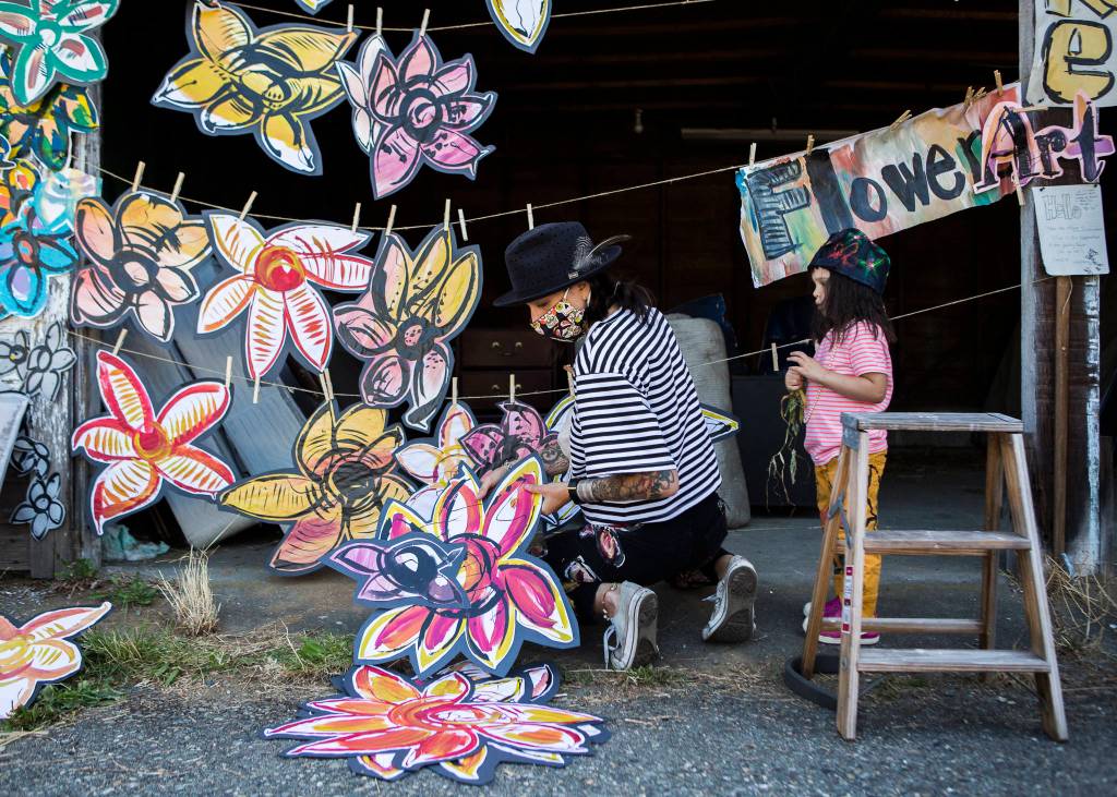 Lennon Wiltbank gets help from her daughter Ottilie Wiltbank, 2, hanging up new flower paintings for admirers to take for free. (Olivia Vanni / The Herald)