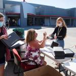 Sheryl Wark stacks computers as Stanwood Highs Renee Herigstad (center) hands a Chromebook to junior Savannah Wickman on Wednesday in Stanwood. Students in the district will be learning online. (Andy Bronson / The Herald)