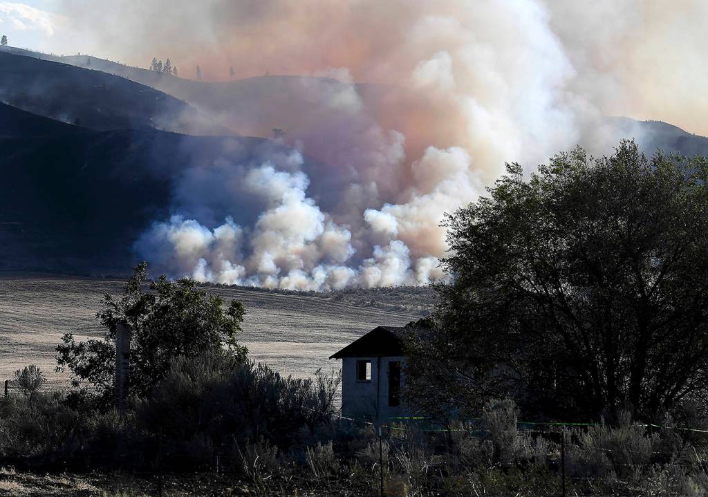 Late afternoon light catches smoke from the Cold Springs Canyon Pearl Hill Fire near a structure that appeared to be empty long before the fire on Monday near Omak. (Tyler Tjomsland/The Spokesman-Review via AP)
