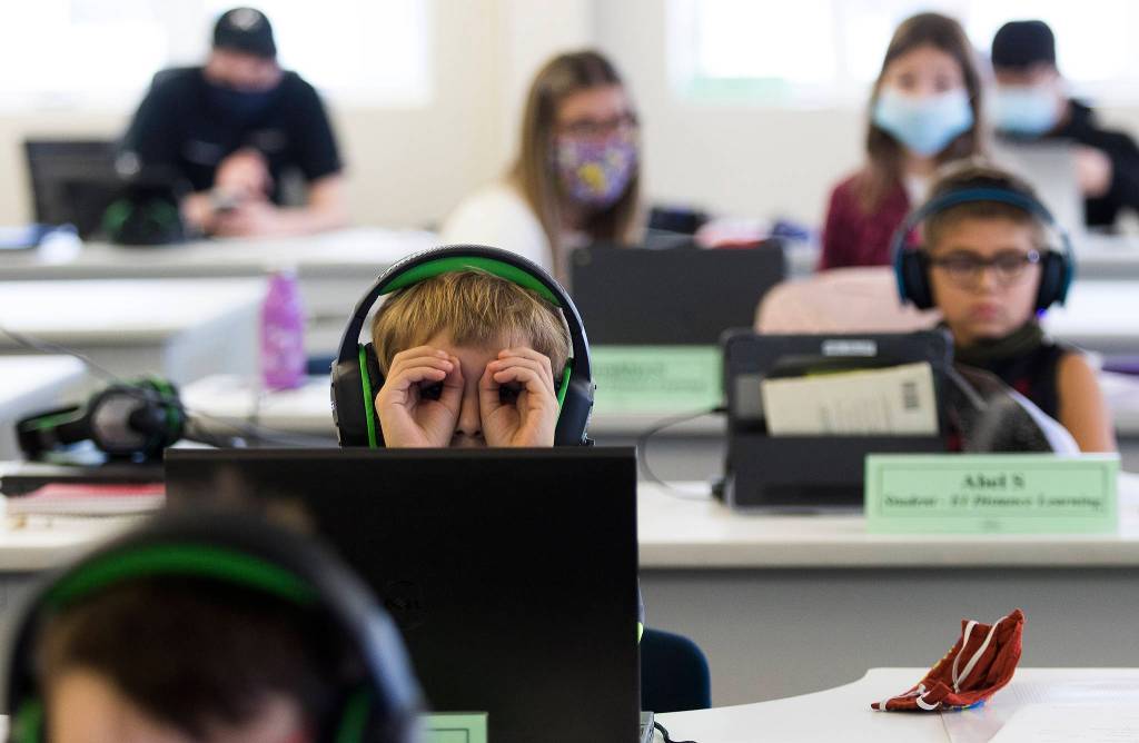 Mason Van Acker makes binoculars of his hands while watching a Zoom class on his computer at Electroimpact in Mukilteo. (Andy Bronson / The Herald)