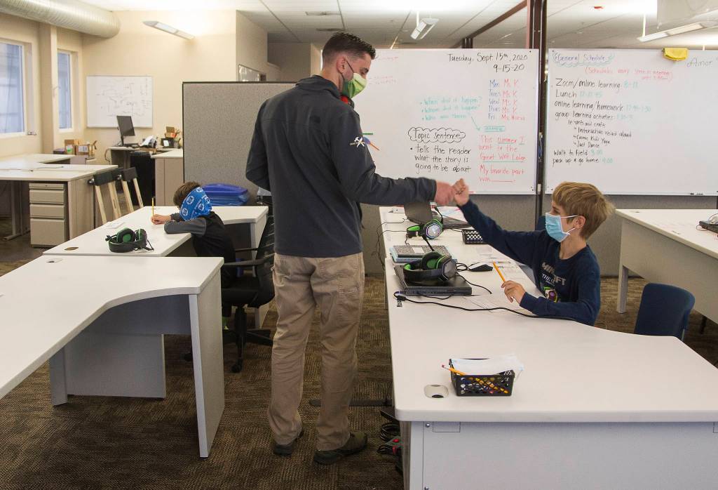 Tom Van Acker gives his son, Mason, a fist bump as he heads to work in another part the building after dropping off his sons at a classroom set up at Electroimpact in Mukilteo. Declan, his other son, is at left. (Andy Bronson / The Herald)