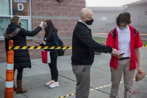 Dean of Students Jeff Latta, center, helps a student through their online health questionnaire while Athletic Director Cassie Snell, left, checks a students temperature before the start of class at Archbishop Murphy on Tuesday, Oct. 6, 2020 in Everett, Wa. (Olivia Vanni / The Herald)