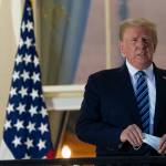 President Trump holds his face mask as he stands on the Blue Room Balcony upon returning to the White House on Monday, in Washington, after leaving Walter Reed National Military Medical Center, in Bethesda, Md. (Alex Brandon / Associated Press)