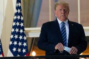 President Donald Trump holds his face mask as he stands on the Blue Room Balcony upon returning to the White House Monday, Oct. 5, 2020, in Washington, after leaving Walter Reed National Military Medical Center, in Bethesda, Md. Trump announced he tested positive for COVID-19 on Oct. 2. (AP Photo/Alex Brandon)