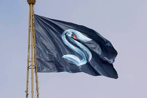 A flag with the new logo for the newly-named Seattle NHL team, the Seattle Kraken, flies atop the iconic Space Needle Thursday, July 23, 2020, in Seattle. The hockey expansion franchise unveiled its nickname Thursday, ending 19 months of speculation about whether the team might lean traditional or go eccentric with the name for the league's 32nd team. Seattle's colors are a deep dark blue with a lighter shade of blue as a complement. (AP Photo/Elaine Thompson)