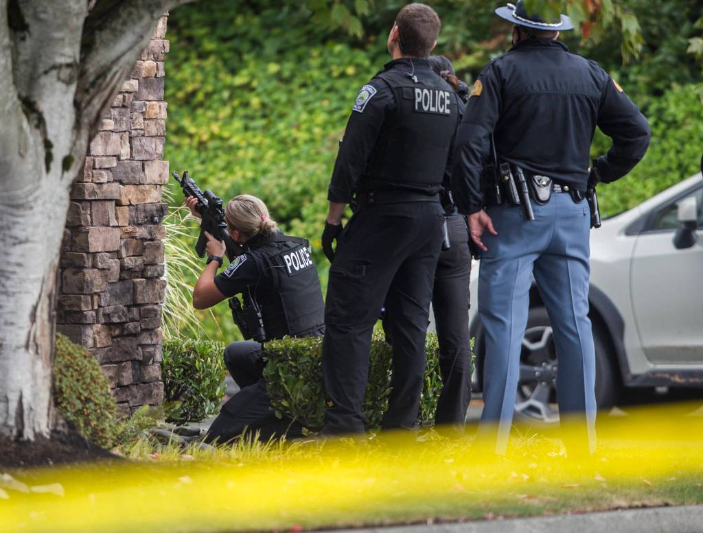 A police officer looks through a scope at a carjacking suspect on Wednesday near Mill Creek. (Olivia Vanni / The Herald)