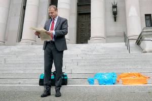 Initiative promoter Tim Eyman reads a newspaper article from the year 2000 about his long-running campaign for $30 car tabs as he waits to talk to reporters, Thursday, Oct. 15, 2020, in front of the Temple of Justice at the Capitol in Olympia, Wash. The Washington Supreme Court on Thursday unanimously struck down Eyman's Initiative 976, a measure that would have steeply discounted the price of car registrations at $30 while gutting transportation budgets across Washington state. (AP Photo/Ted S. Warren)
