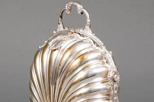 This silver-plated serving piece is called a box but it doesn't look like one. It held English biscuits, but if the sides opened, the cookies inside would fall down. Each of the shell-shaped bowls had a hinged, pierced flap that kept the heat and the biscuits in place when the sides were opened and became flat bowls to serve the cookies. The flaps are often missing when the biscuit box is sold.-