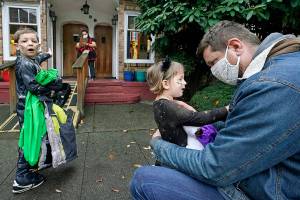 Alex Stonehill gets a goodbye from his daughter Helenore, 2, as her brother Malcolm, 4, motions to a friend arriving at the Community Day Center for Children on Thursday, Oct. 29, 2020, in Seattle. As more families make the jump back to group day care this fall in an attempt to restart lives and careers, many parents, pediatricians and care operators are finding that new, pandemic-driven rules offer a much-needed layer of safety but also seem incompatible with the germy reality of childhood.  (AP Photo/Elaine Thompson)