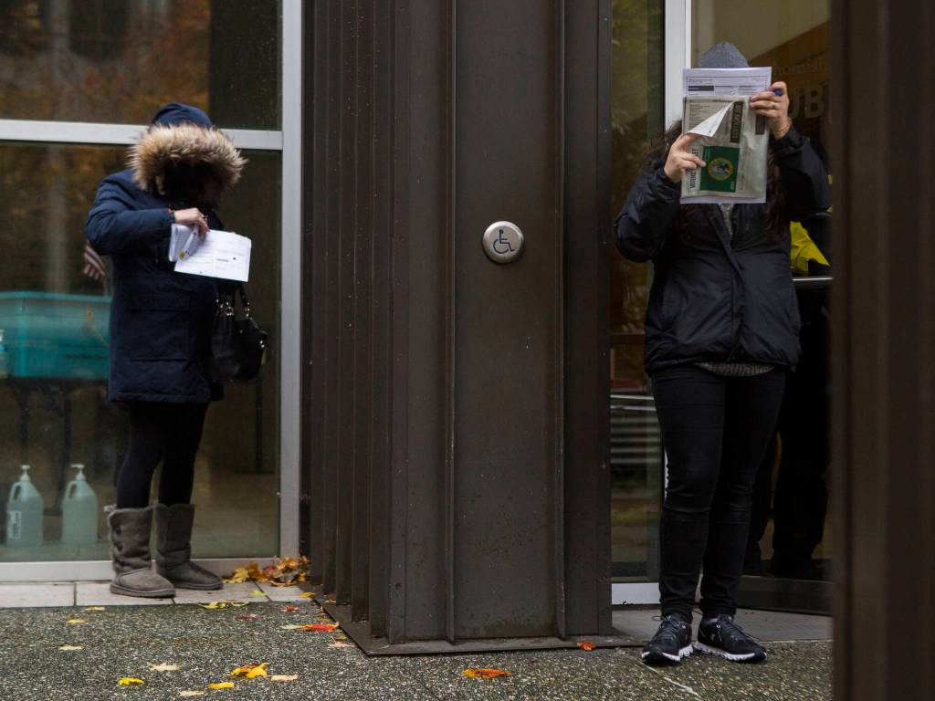 People stand outside in the rain and fill out their ballots on Tuesday in Everett. (Olivia Vanni / The Herald)