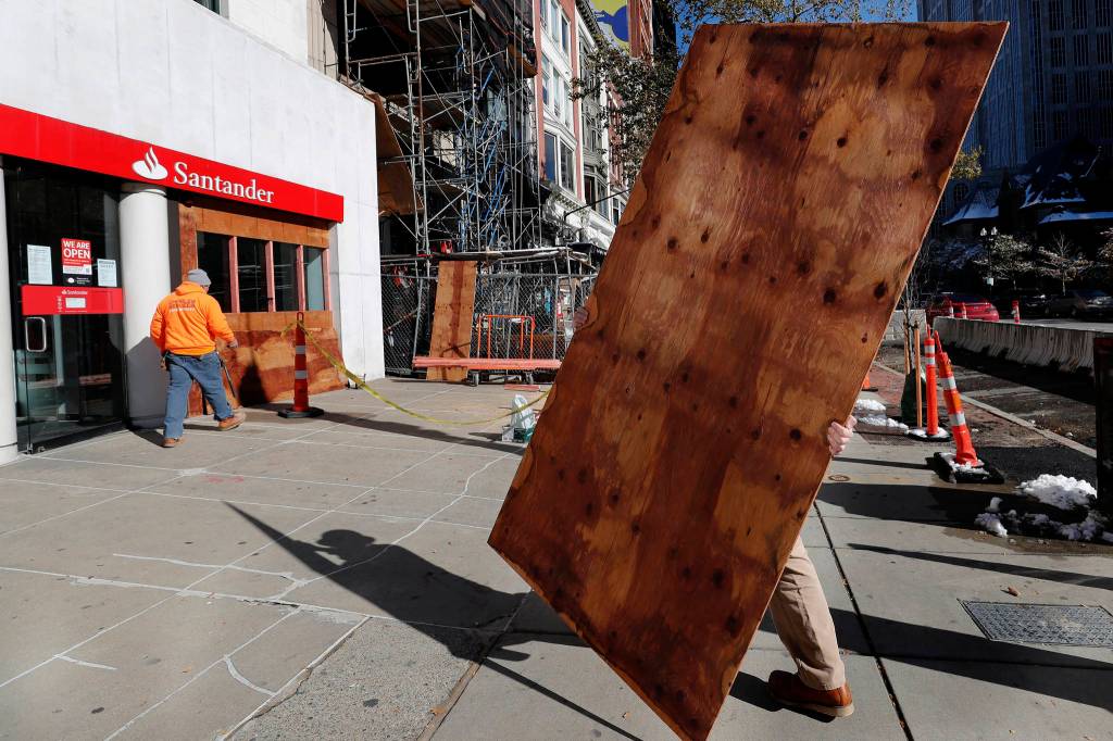 Workers board up the windows of a Santander Bank branch on Boylston Street, Saturday, Oct. 31, 2020, in Boston. (AP Photo/Michael Dwyer)