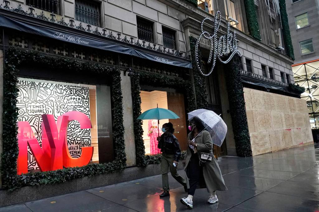 People walk past a partially-boarded up Saks Fifth Avenue, Sunday, Nov. 1, 2020, in New York. Retailers including Nordstrom, Tiffany and Saks are planning to board up their windows or add extra security personnel in some of their locations ahead of the contentious presidential election on Tuesday. (AP Photo/Kathy Willens)