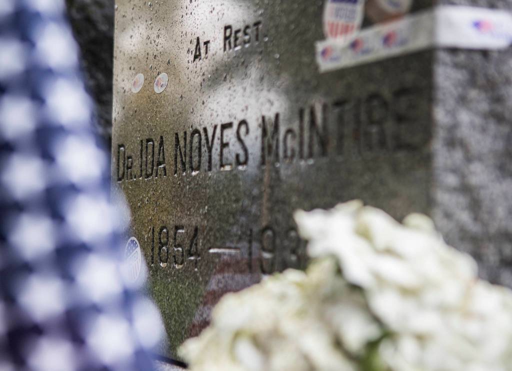 The gravestone of suffragist Dr. Ida Noyes McIntire, surrounded by flowers and covered in I voted stickers, at the Evergreen Cemetery on Wednesday in Everett. (Olivia Vanni / The Herald)