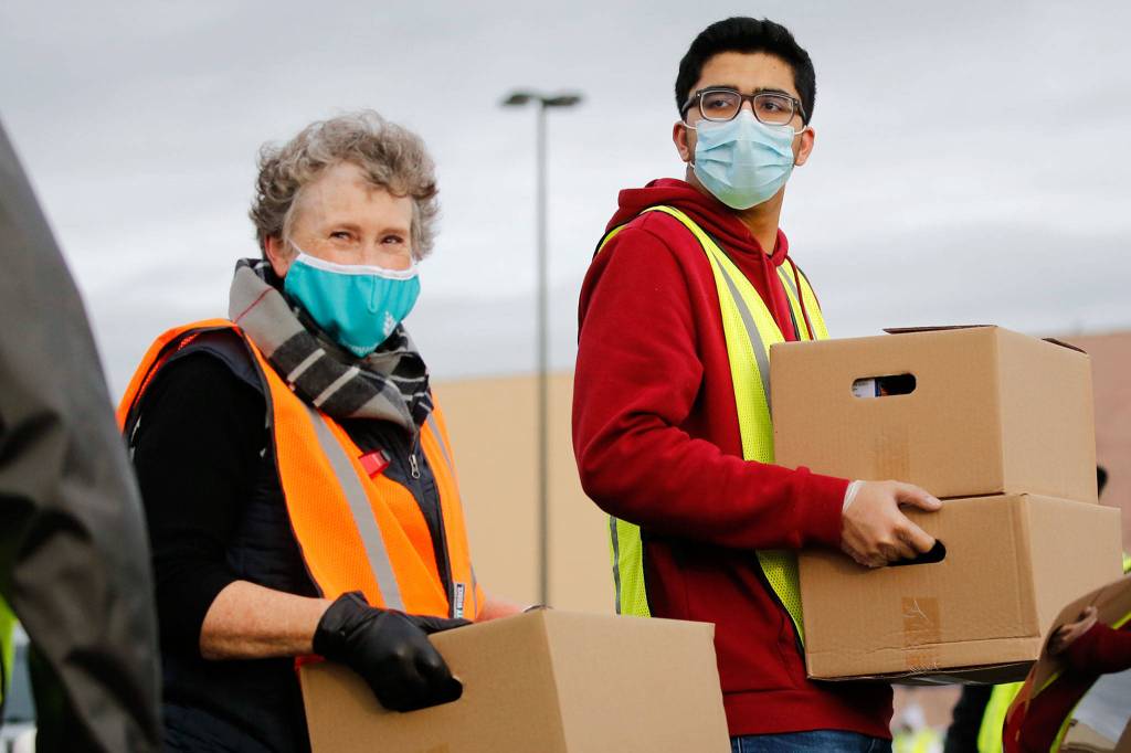 Mary Bickmell (left) and Shivam Vahadari carry boxes for loading Friday during a drive-thru food distribution at Everett Mall. (Kevin Clark / The Herald)