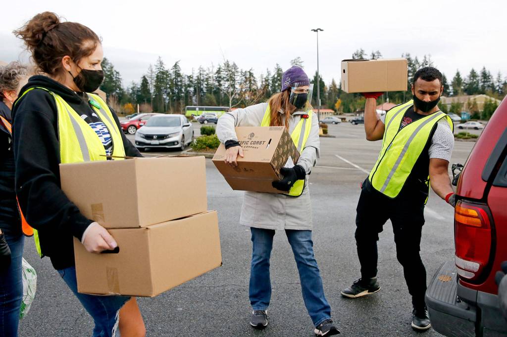 Ashley Zwiefelhofer, (left - right) Christina Broadwin and James Shiriwasto load food stuffs Friday during a drive-thru distribution at Everett Mall. (Kevin Clark / The Herald)