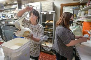 Sarah Calvo pours icing on to a cinnamon roll at the Maltby Cafe while Kylie King checks take out orders on Thursday, Dec. 3, 2020 in Maltby, Washington. A GoFundMe fundraising page continues to grow, raising more than $80,000 from 1,200 people in just a few days. Owners Tana Baumler and Sandra Albright thought they were going to closed before the website donations made them pause their decision. (Andy Bronson / The Herald)