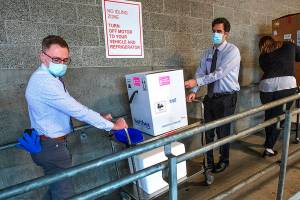 University of Washington Medical Center Montlake campus pharmacy administration resident Derek Pohlmeyer, left, and UWMC pharmacy director Michael Alwan transport a box containing Pfizer-BioNTech COVID-19 vaccines toward a waiting vehicle headed to the UW Medical Center's other hospital campuses on Monday, Dec. 14, 2020, in Seattle. (Mike Siegel/The Seattle Times via AP, Pool)