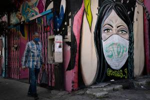 A man wearing a face mask walks past a mural Thursday, Oct. 1, 2020, in South Central Los Angeles. California's plan to safely reopen its economy will begin to require counties to bring down coronavirus infection rates in disadvantaged communities that have been harder hit by the pandemic. The complex new rules set in place an "equity metric" that will force larger counties to control the spread of the virus in areas where Black, Latino and Pacific Islander groups have suffered a disproportionate share of the cases due to a variety of socioeconomic factors. (AP Photo/Jae C. Hong)